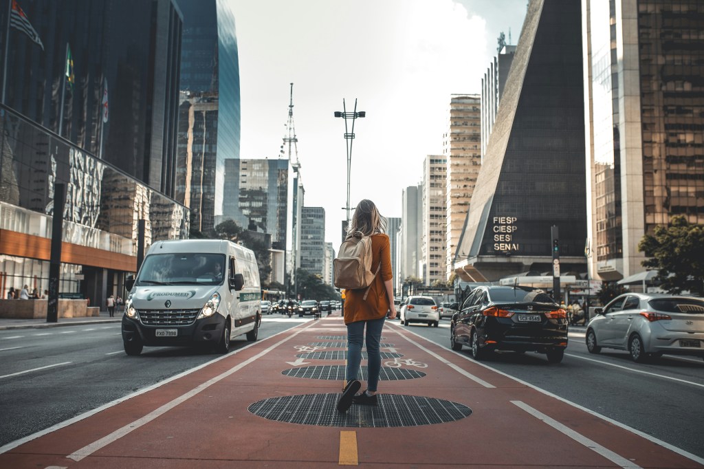 A woman standing in the middle of a busy street with a backpack